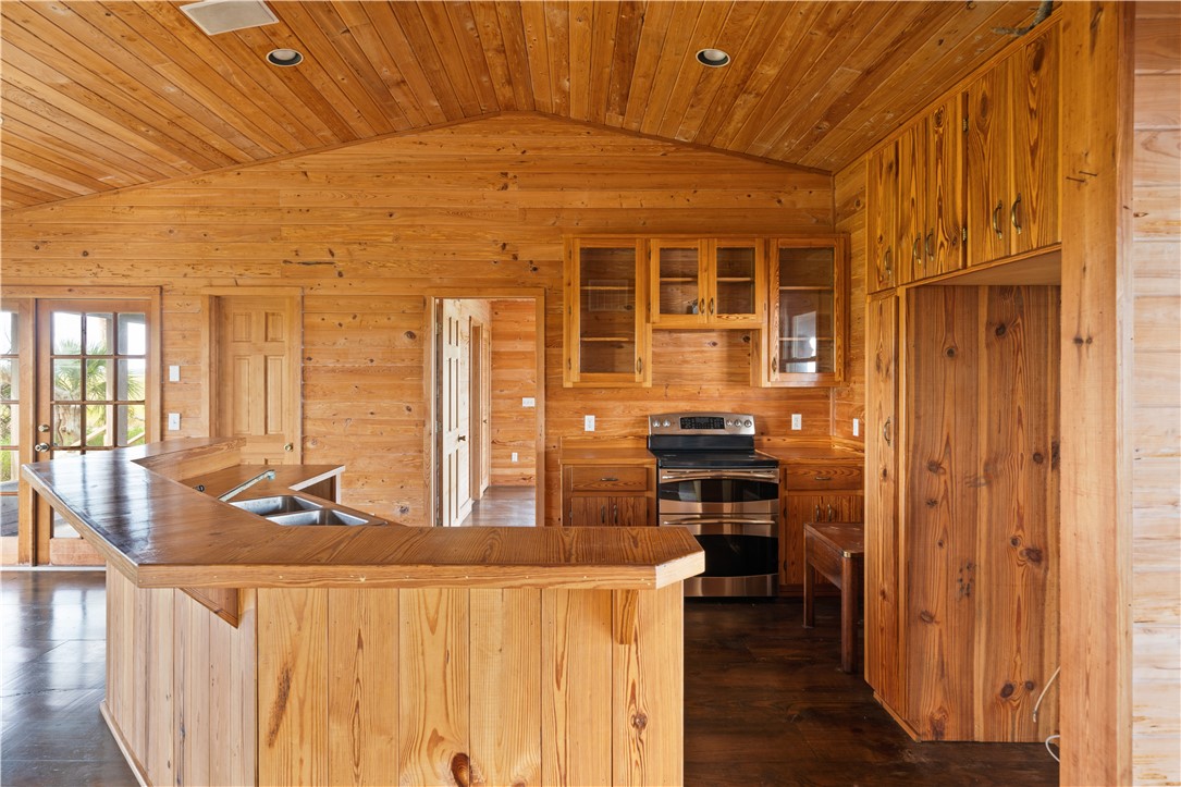 Rustic wood-paneled kitchen with a large double-sink island and stainless steel range.