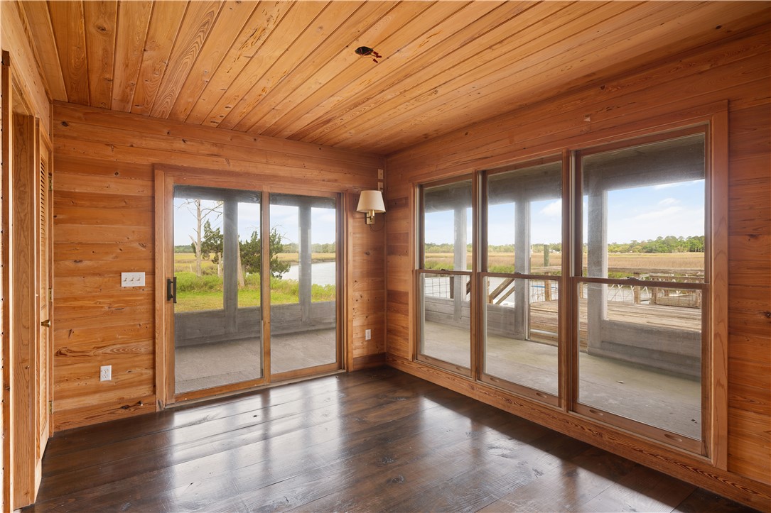 Wood-paneled room with dark floors and wide windows overlooking a deck, water, and marshland.