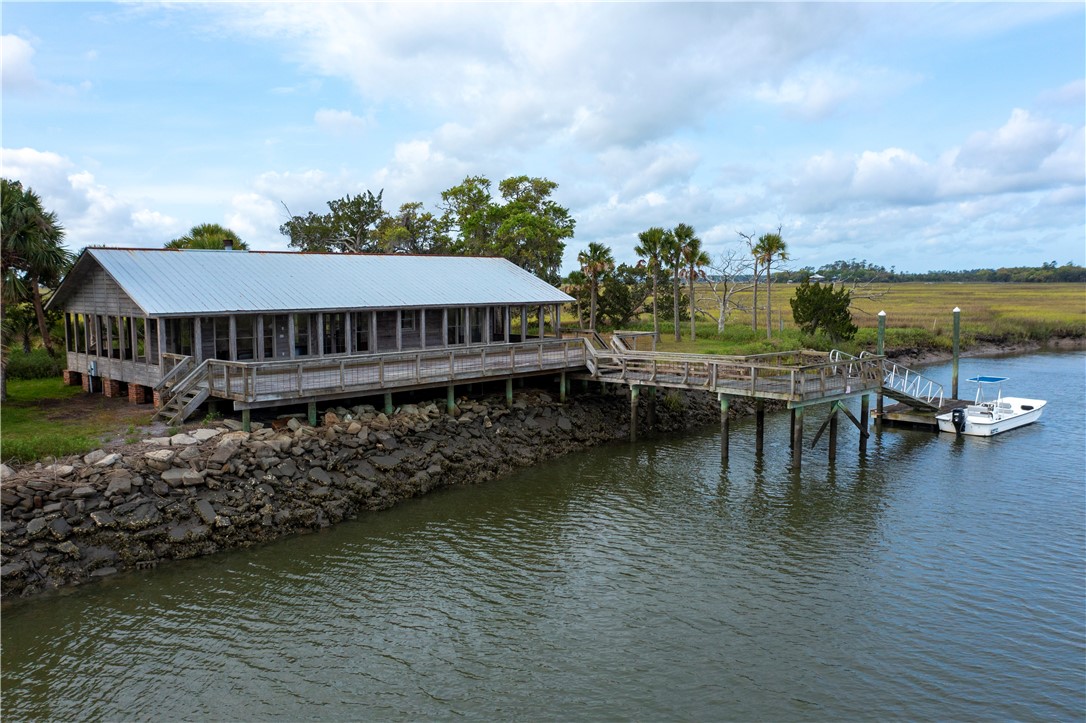 Waterfront pavilion and long wooden dock extend over a tidal creek beside coastal marsh.