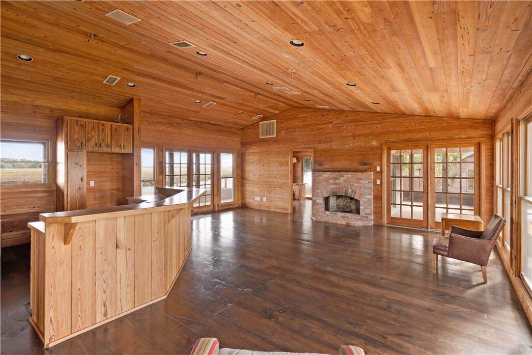 Wood-paneled living room with a large bar counter, brick fireplace, and glass doors facing marshland.