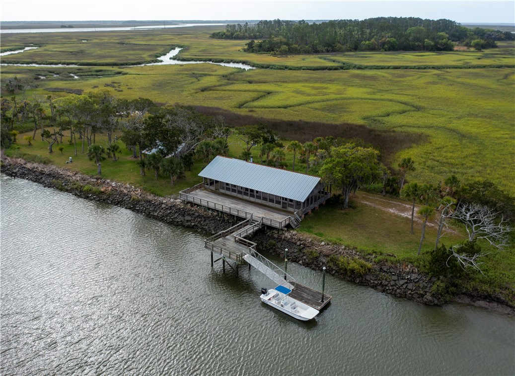 Waterfront building with a long wooden dock and boat beside a coastal marsh.