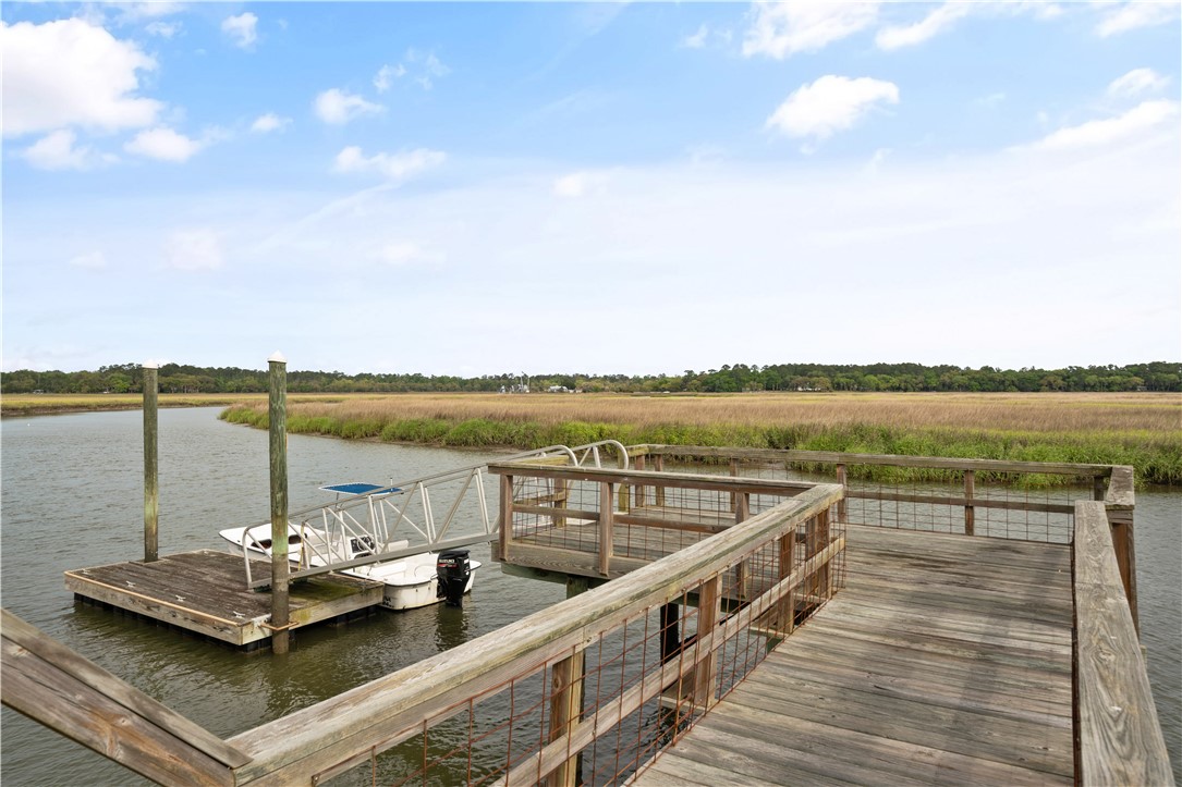 Wooden dock and walkway over a tidal creek, with a small boat beside grassy marshland.