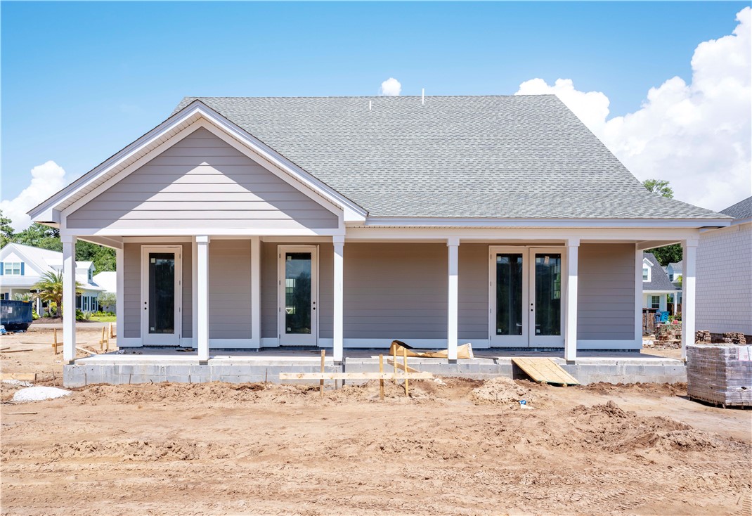 New gray-sided house with a covered porch, exposed foundation, and unfinished dirt yard.