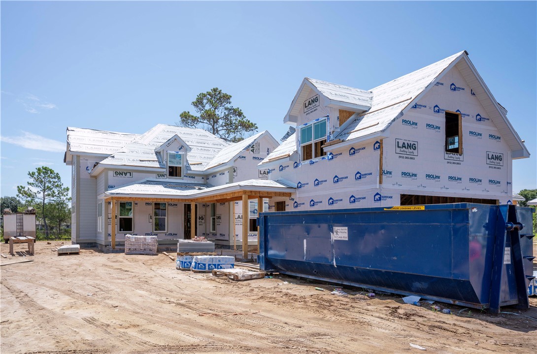 House under construction with exposed house wrap and a large blue dumpster in front.
