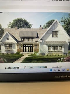 House exterior displayed on a laptop screen, with white gables, stone facade, and front lawn.