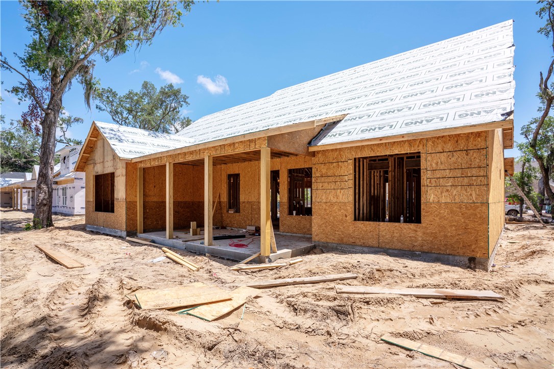 House under construction with exposed wood sheathing, a covered porch, and white roofing underlayment.