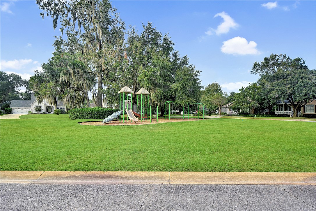 Neighborhood playground on a broad lawn beneath moss-draped oak trees, with homes in the background.