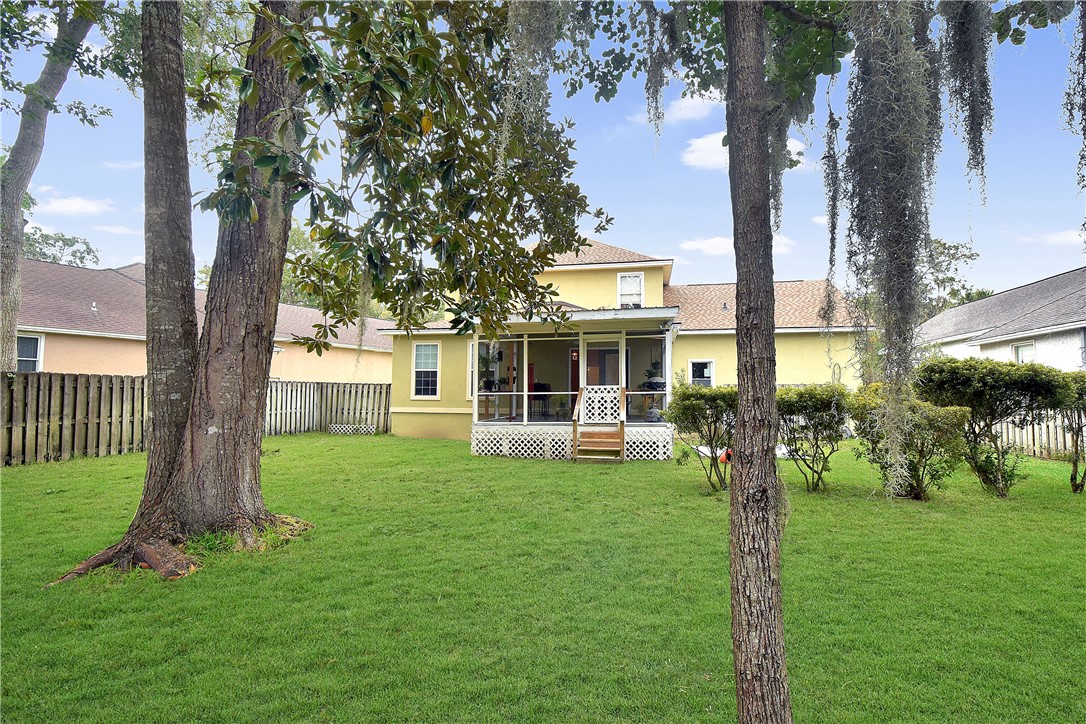 Yellow home with a covered rear porch and broad lawn shaded by mature trees.