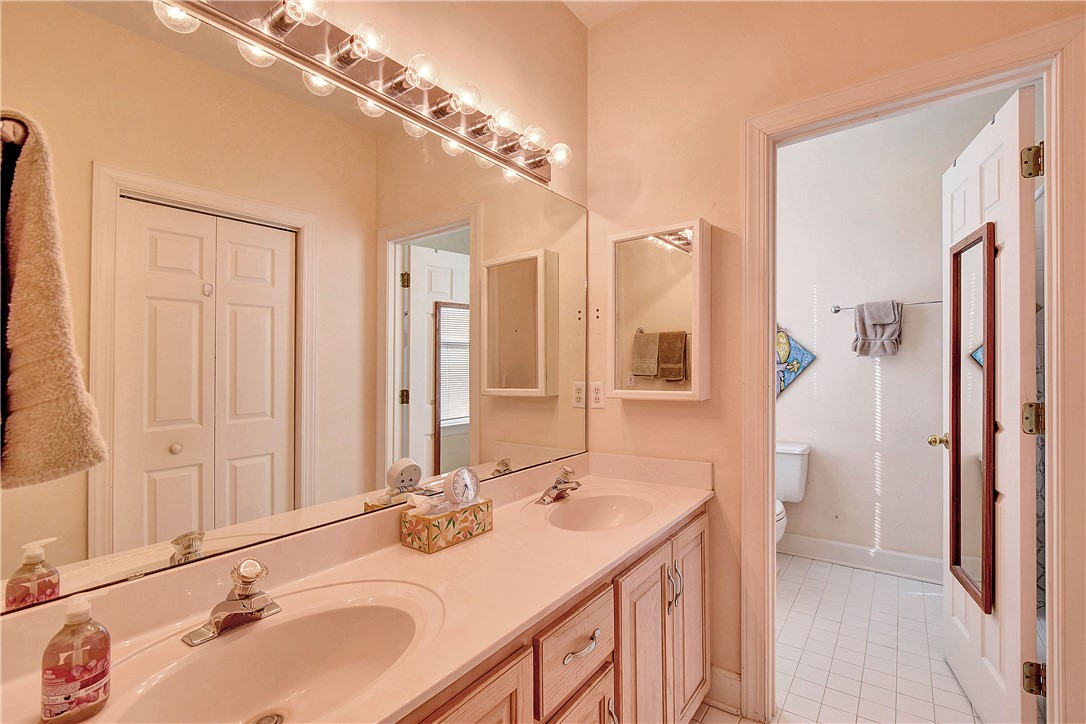 Bathroom with a long double-sink vanity and an open doorway to a separate toilet area.