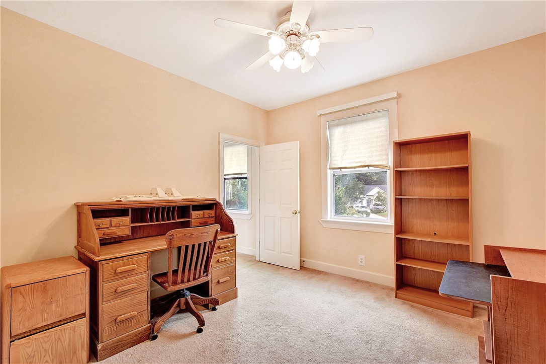 Home office with a wooden roll-top desk, chair, bookcase, and two windows.