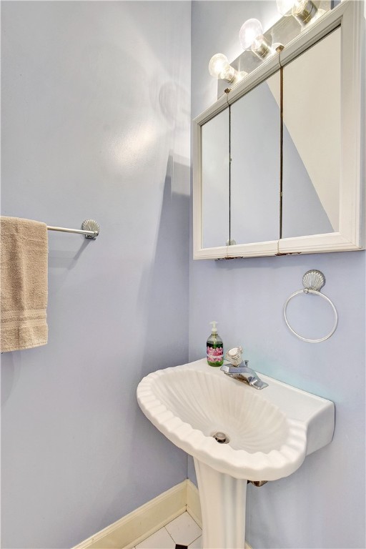 Bathroom with a white scalloped pedestal sink and mirrored cabinet topped by globe lights.