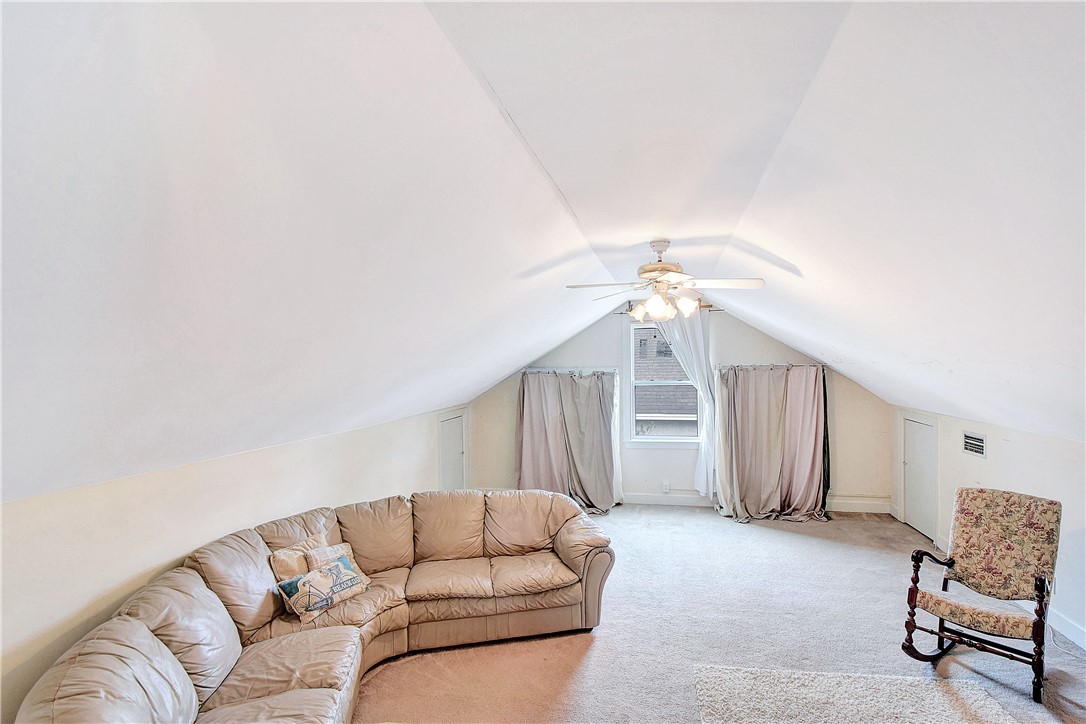 Attic living room with steep sloped ceilings, a beige sectional sofa, and a ceiling fan.