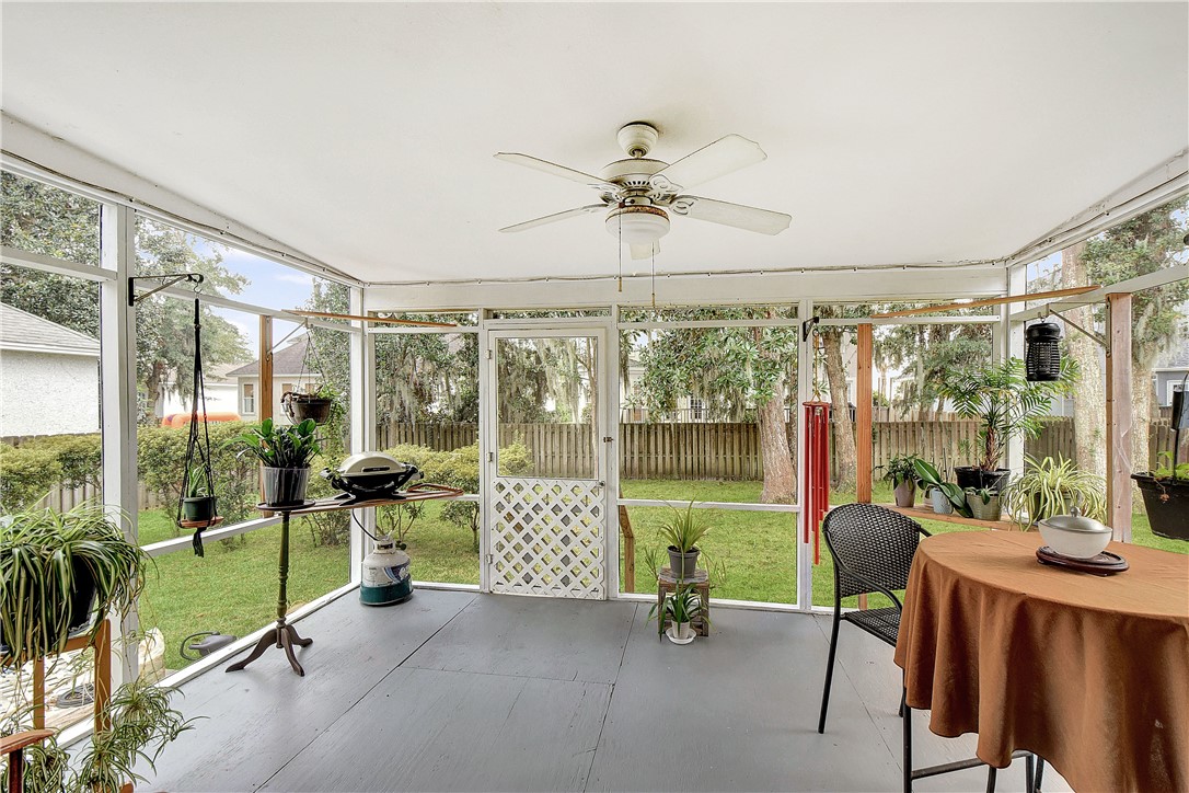 Screened porch with potted plants, a small grill, and a round table overlooking a fenced yard.