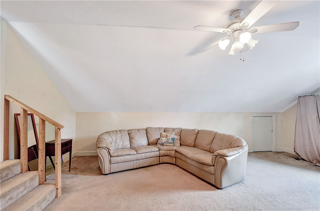 Upstairs living area with a beige sectional sofa, open staircase, and ceiling fan.