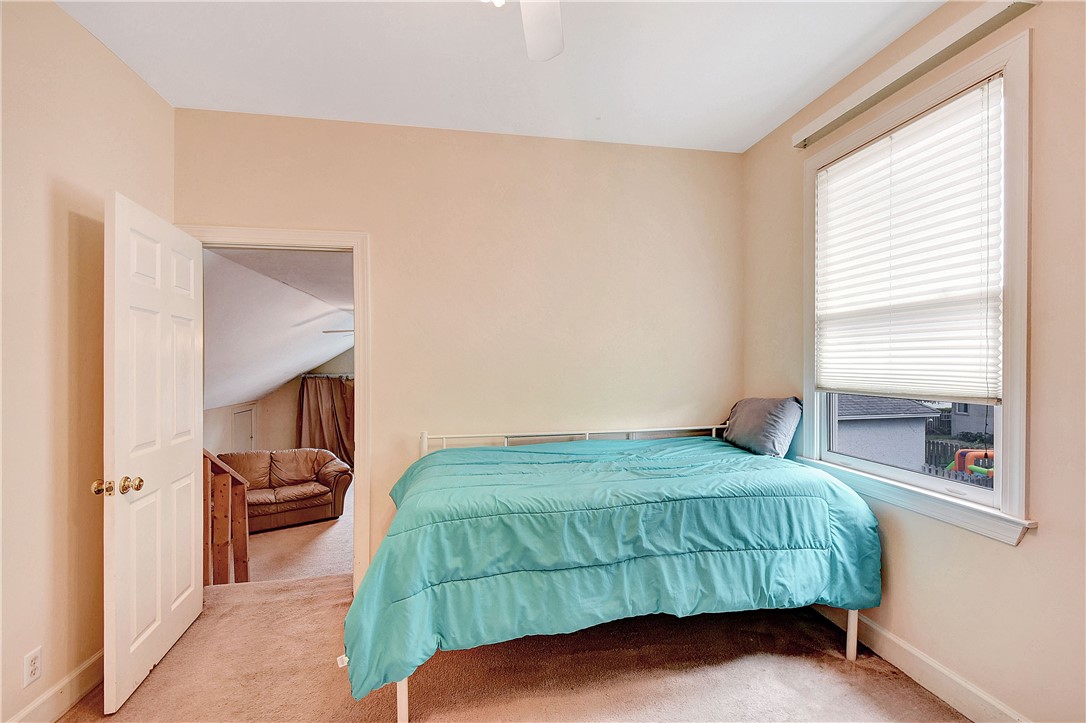 Bedroom with a turquoise-covered bed beside a window with blinds and an open doorway to a sitting area.