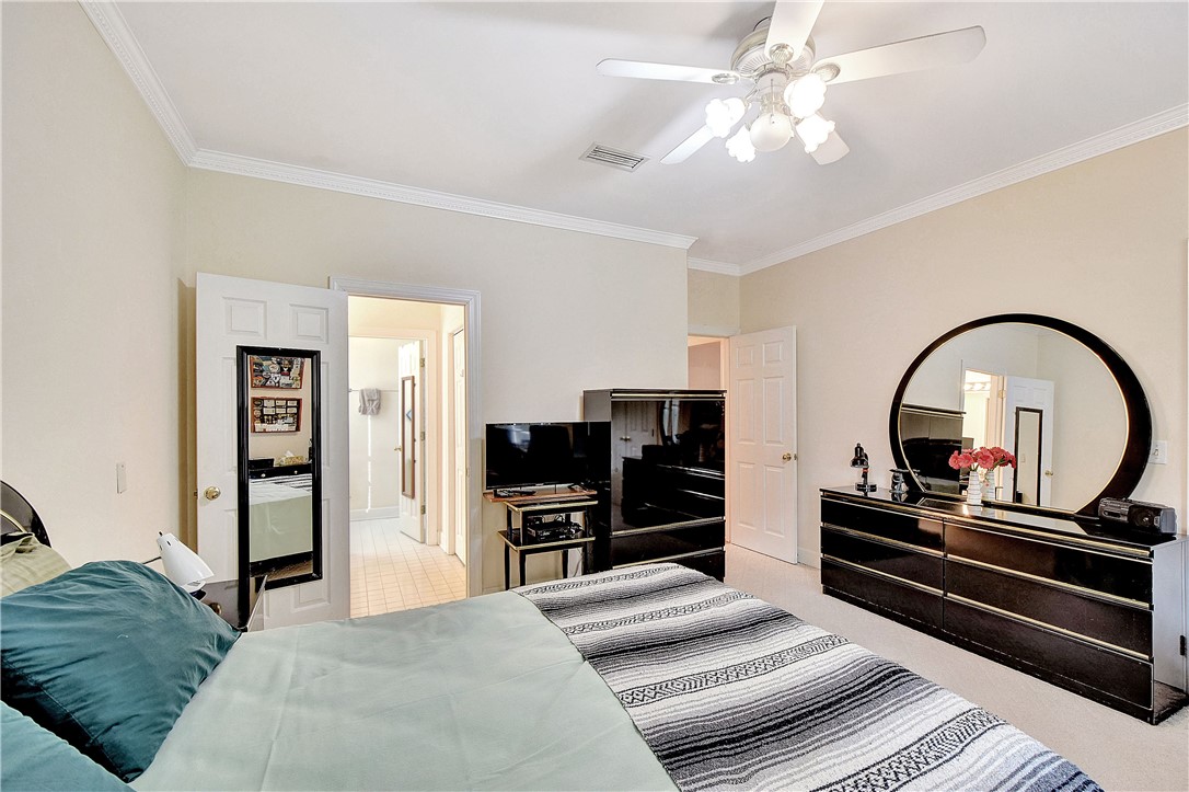 Bedroom with a gray striped bedspread, ceiling fan, dark dressers, and large round mirror.