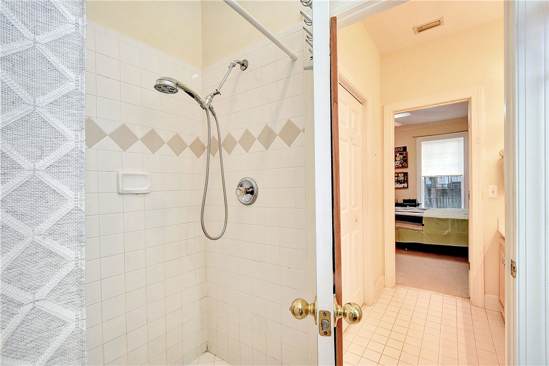 Tiled bathroom shower with a diamond-pattern accent band and open view into a bedroom.