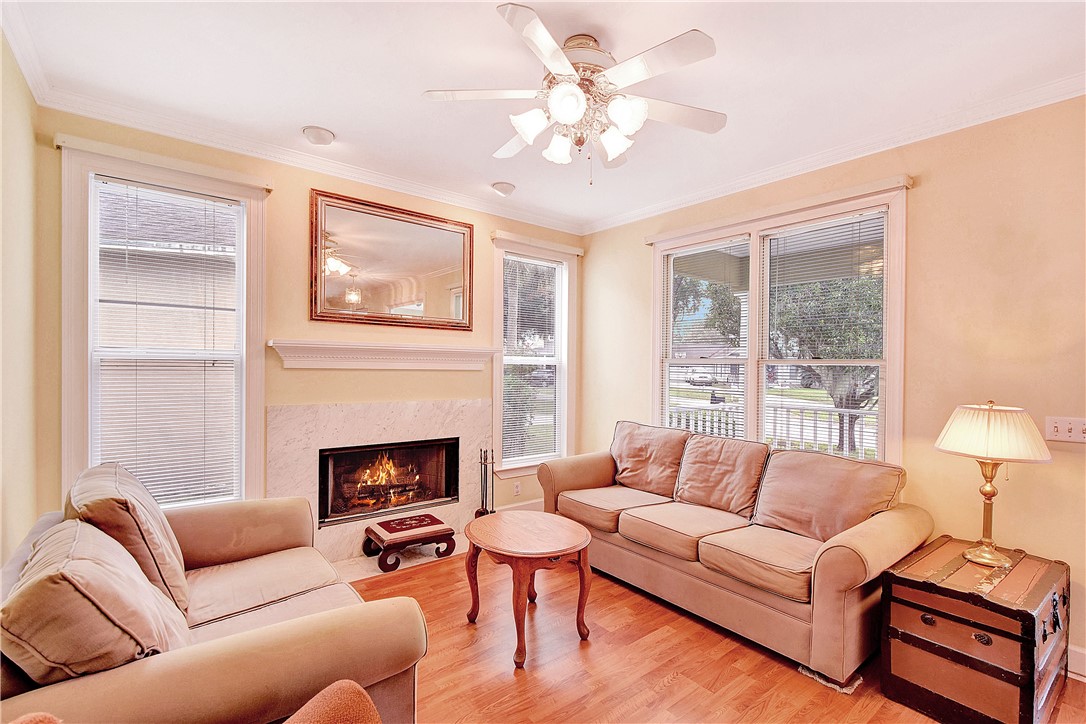 Living room with a lit fireplace, two sofas, hardwood floors, and large windows.