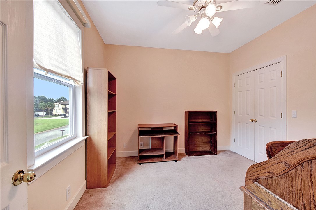 Carpeted bedroom with a large street-facing window, wooden shelving, closet doors, and part of a bed.