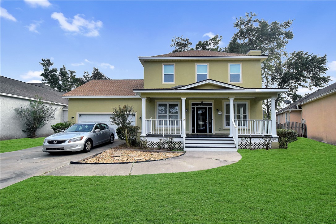 Two-story olive-green home with a covered front porch, attached garage, and broad green lawn.