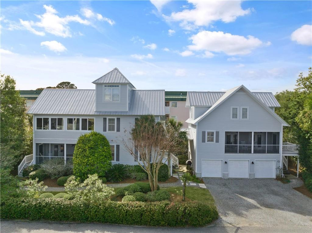 Two adjoining gray homes with metal roofs, covered balconies, and landscaped front yards.