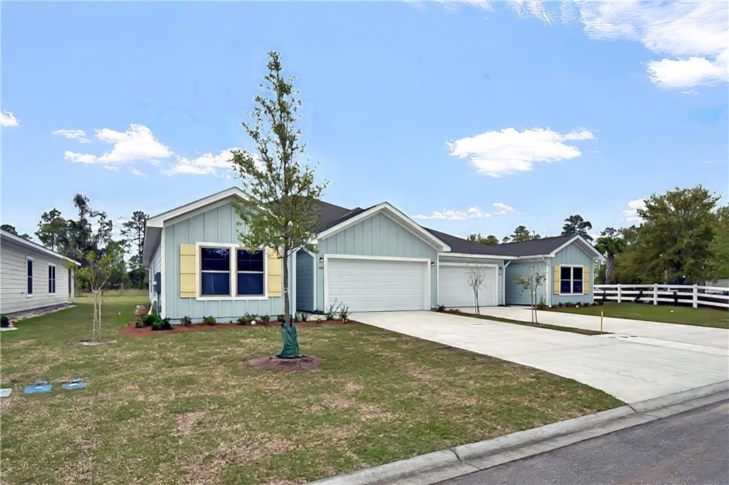 Light blue single-story home with attached garages, broad driveway, lawn, and white fence.