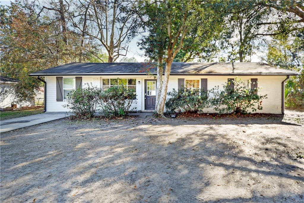 Single-story white ranch house with dark shutters, mature trees, and a sandy front yard.