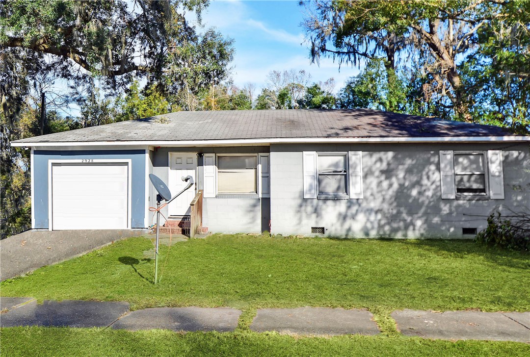 Single-story gray house with a white garage, front lawn, and mature moss-draped trees.