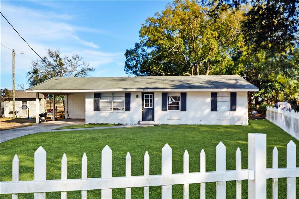 Single-story white house with dark shutters, a covered carport, and a white picket fence.