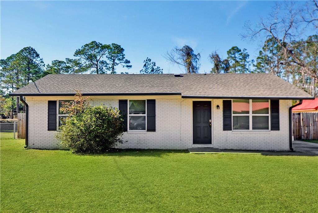 Single-story white brick house with black shutters, a front lawn, and trees behind it.