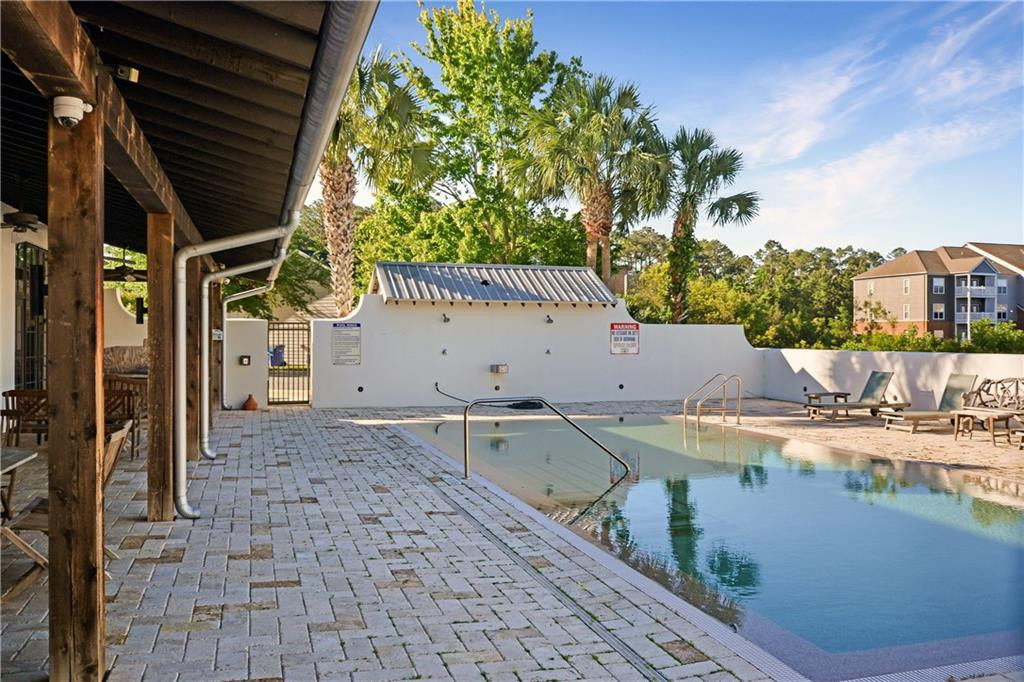 Outdoor swimming pool with a covered wooden pavilion, paved deck, and palm trees.