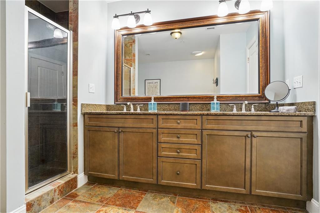 Bathroom with a brown double vanity, large framed mirror, and glass-enclosed tiled shower.