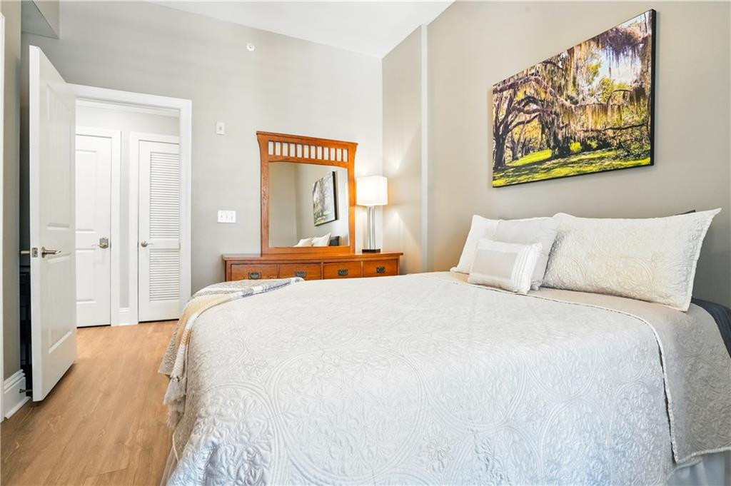 Bedroom with a large white bed, wooden dresser and mirror, and framed landscape art.