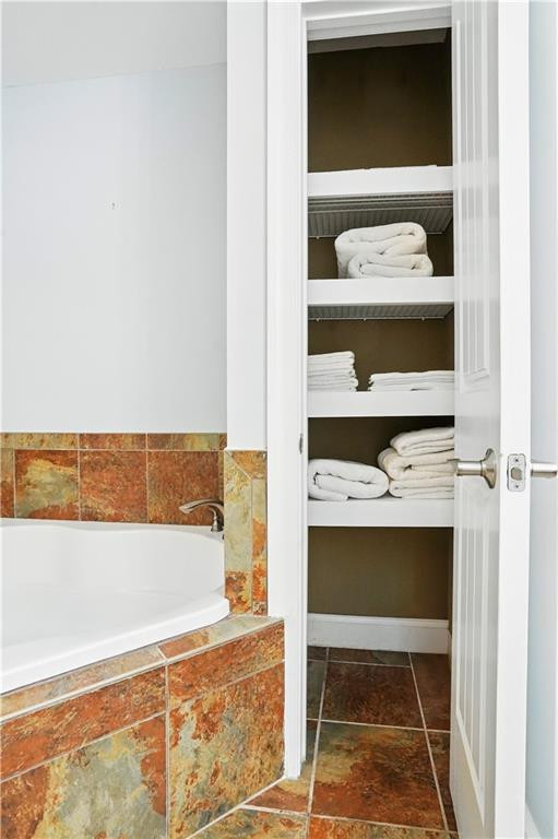 Bathroom with a tiled corner bathtub beside an open linen closet stocked with white towels.