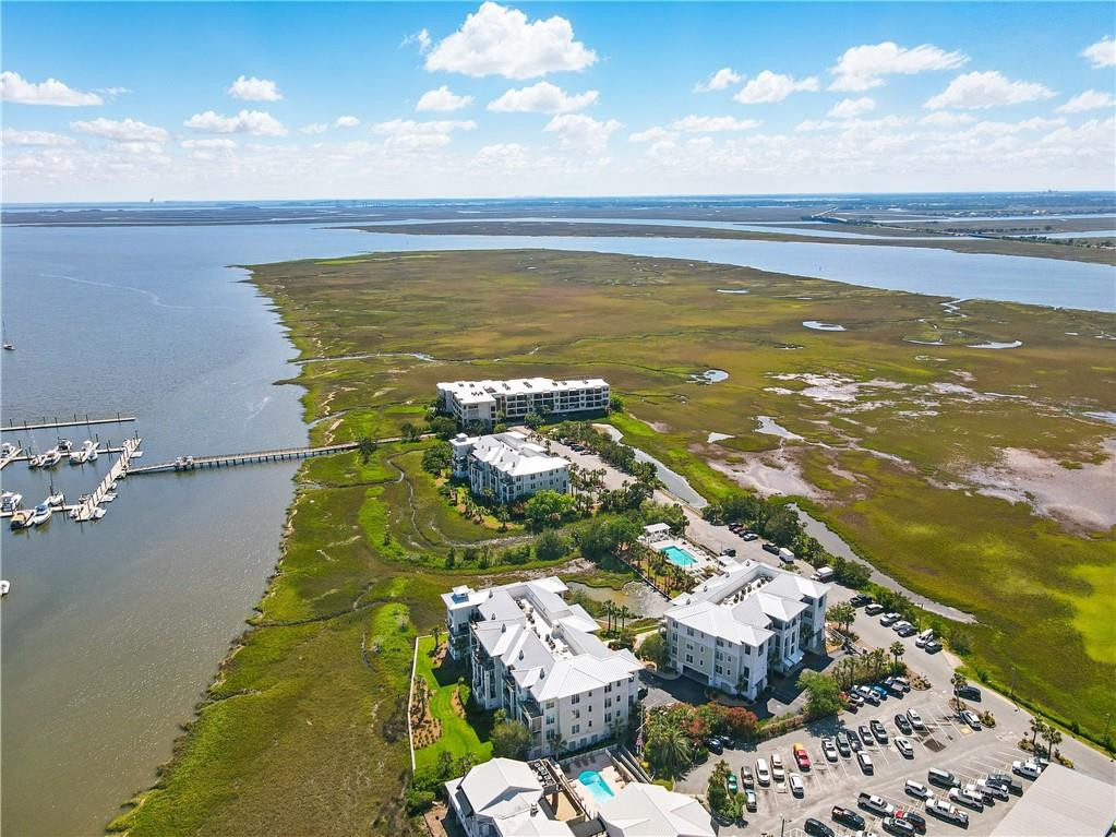 Coastal condominiums beside a broad marsh, with a marina, swimming pool, and parking areas.