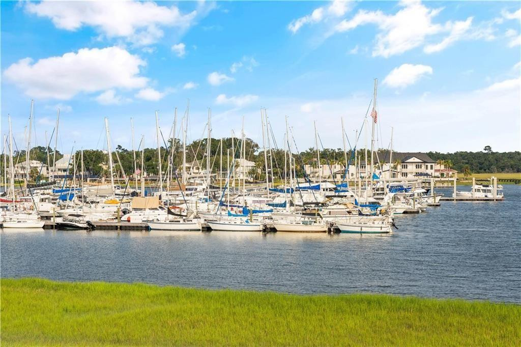 Marina filled with sailboats across calm water, viewed from a grassy waterfront.