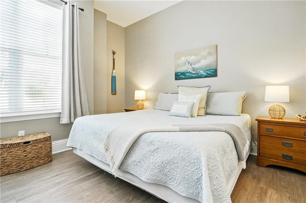 Bedroom with a white quilted bed, sailboat artwork, and a window with blinds and gray curtains.