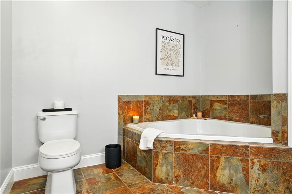 Bathroom with a white bathtub, toilet, and mottled stone tile surround and floor.