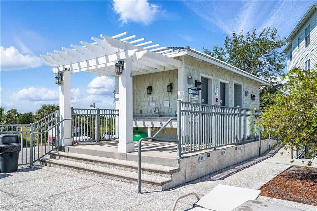 Poolside building with a white pergola, concrete steps, and metal railings.