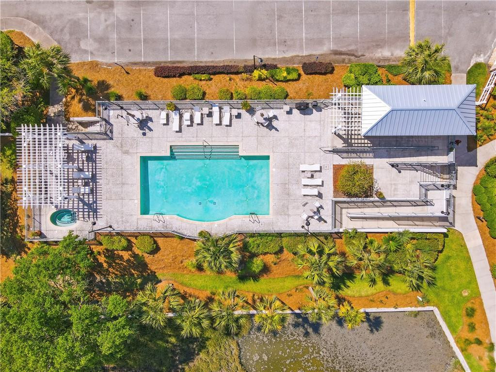 Aerial view of a turquoise pool surrounded by a paved deck, lounge chairs, and pergolas.