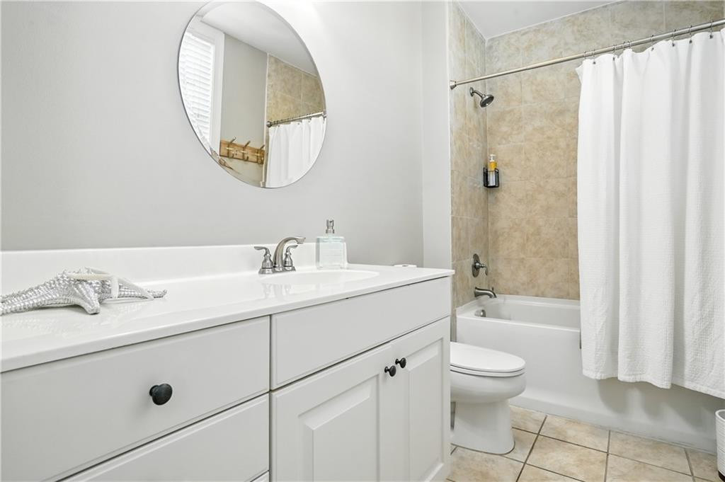 Bathroom with a white vanity, round mirror, and beige-tiled tub-shower.