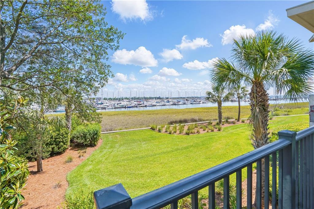 Balcony overlooks a marina and marsh, framed by palms and a waterfront lawn.