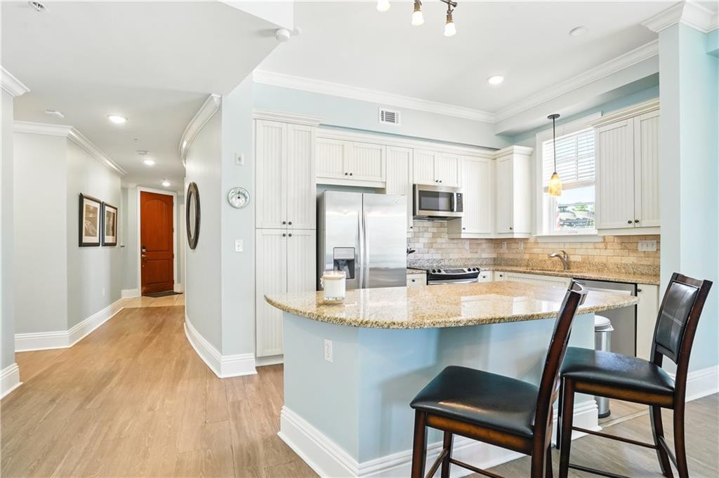 Kitchen with a granite island, white cabinetry, stainless steel appliances, and a hallway beyond.