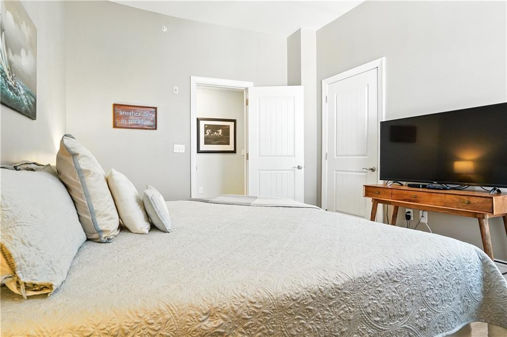 Furnished bedroom with a white quilted bed and television on a wooden console.