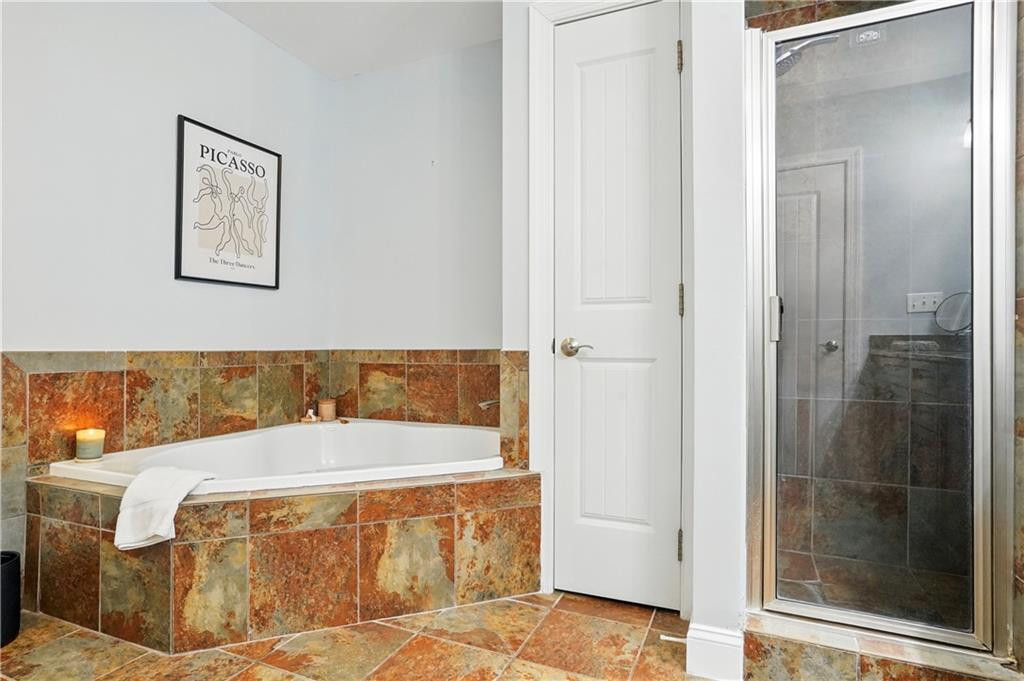 Bathroom with a white soaking tub, multicolored stone tile, and glass-enclosed shower.