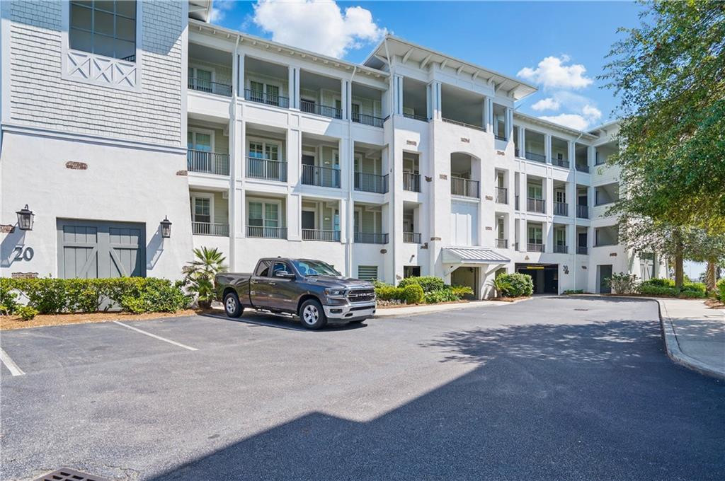 White multi-story condominium building with stacked balconies beside a paved parking area.