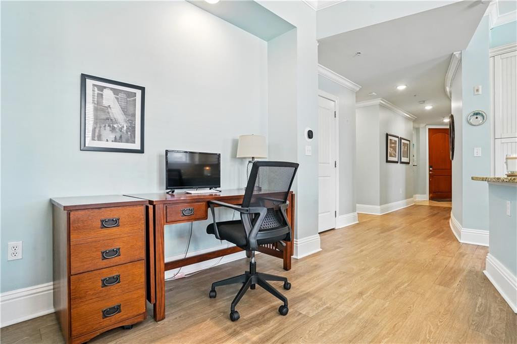 Furnished home office with a wooden desk and black chair beside a long hallway.