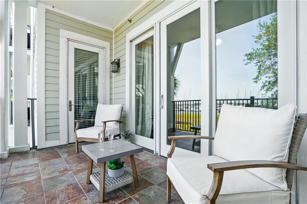 Covered patio with white-cushioned chairs, tiled floor, and marina glimpsed beyond the railing.