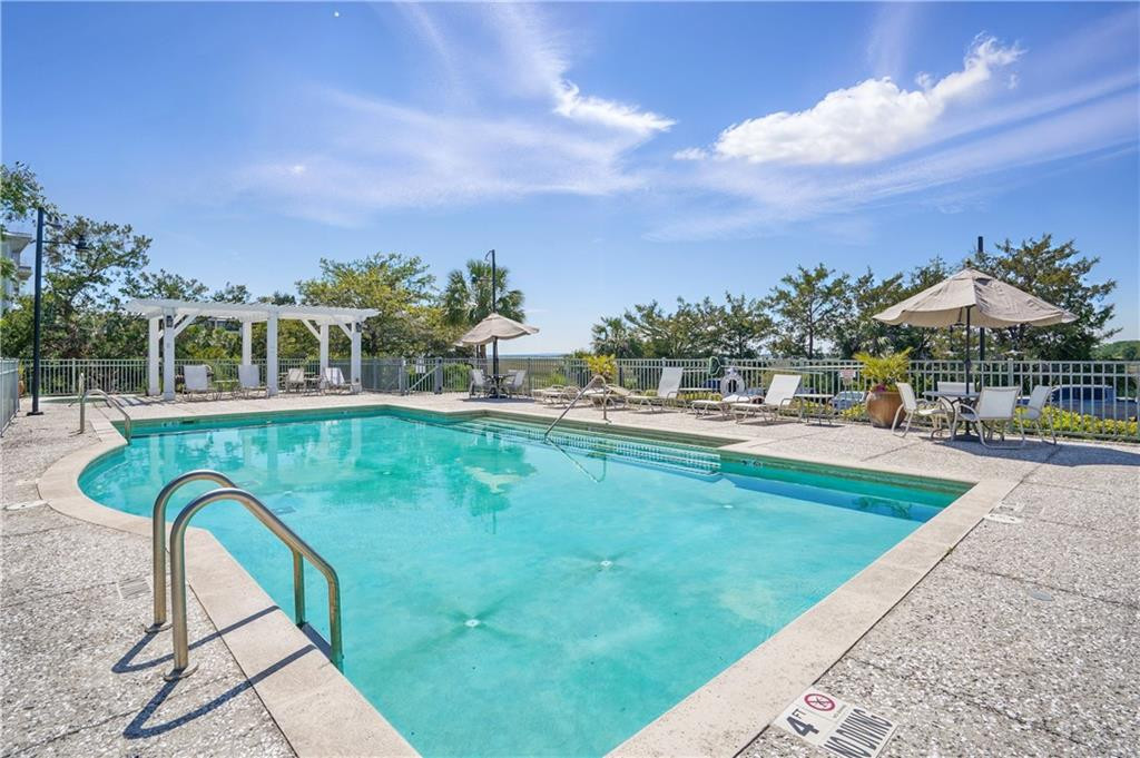 Outdoor swimming pool with deck chairs, umbrellas, and a white pergola.