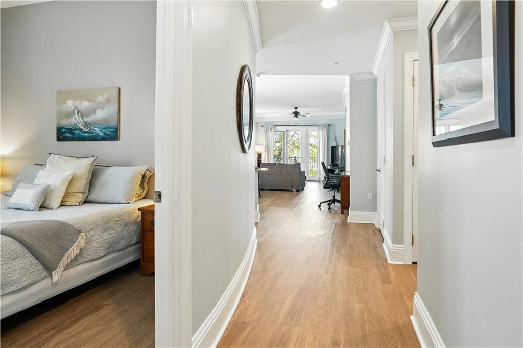Hallway with light wood floors leads past a furnished bedroom to a bright living area.
